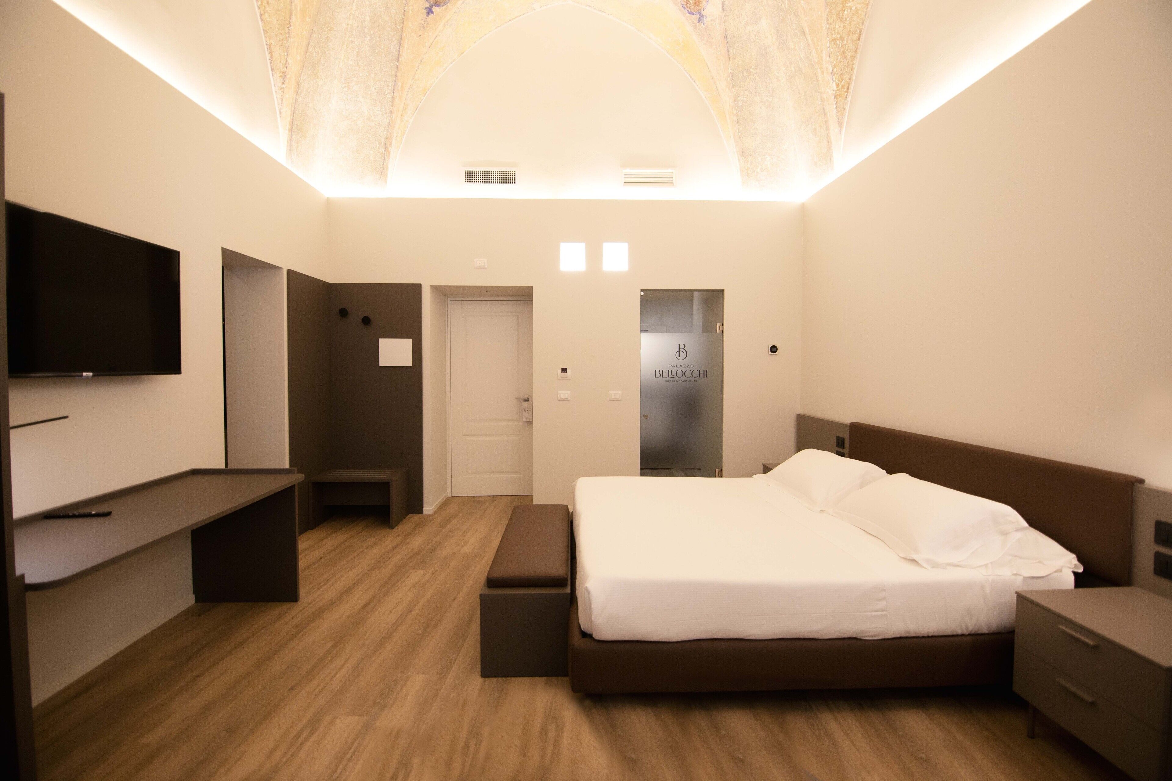 A modern bedroom with a bed, bedside tables, a bench, a TV, and a door.