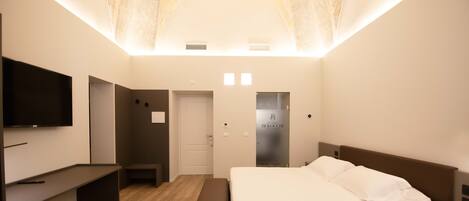 A modern bedroom with a bed, bedside tables, a bench, a TV, and a door.