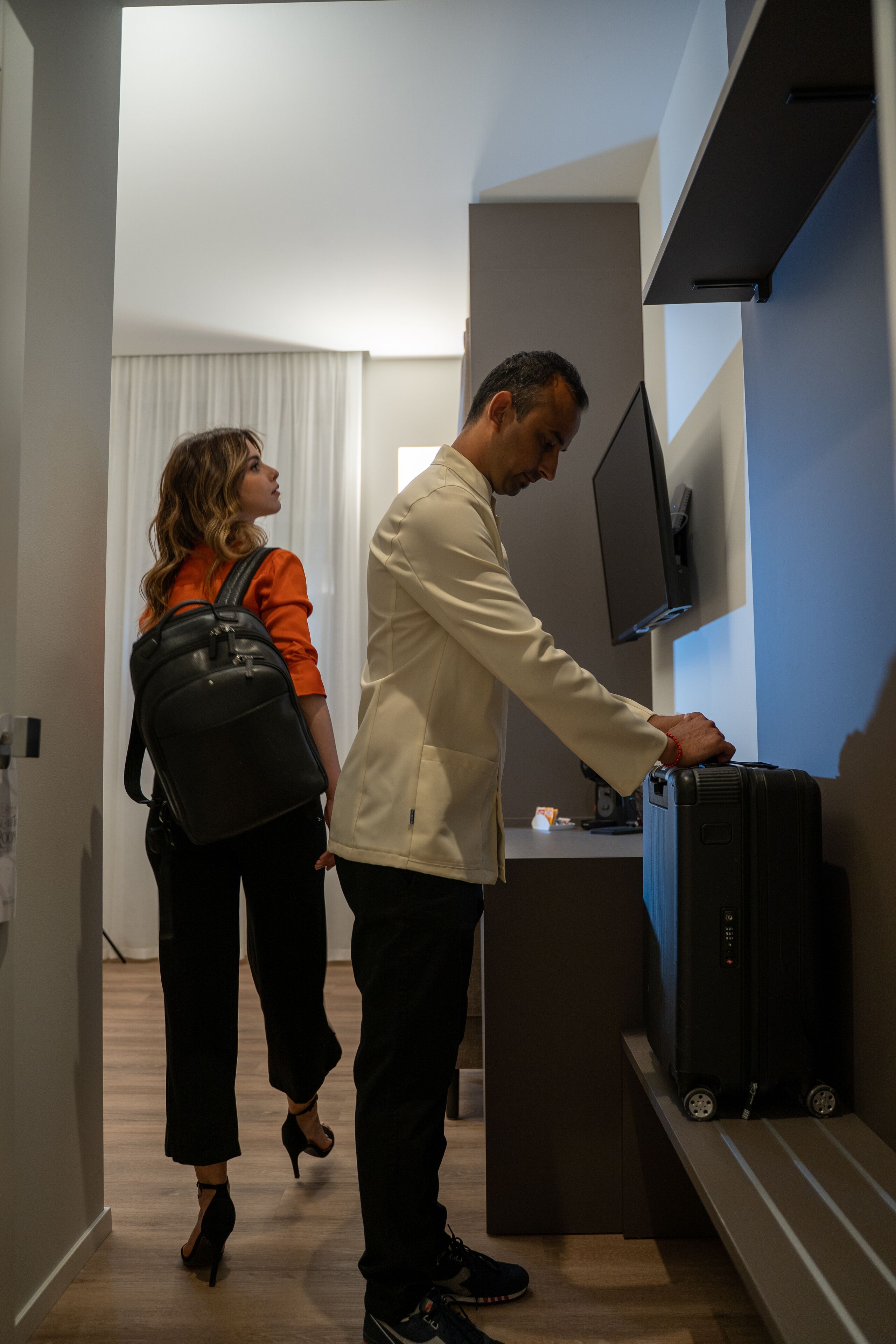 A man adjusting a television in a hotel room with a desk and a chair.