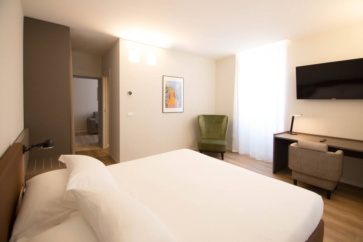 Habitación de hotel con cama, escritorio, silla, televisor y puerta que da a otra habitación.