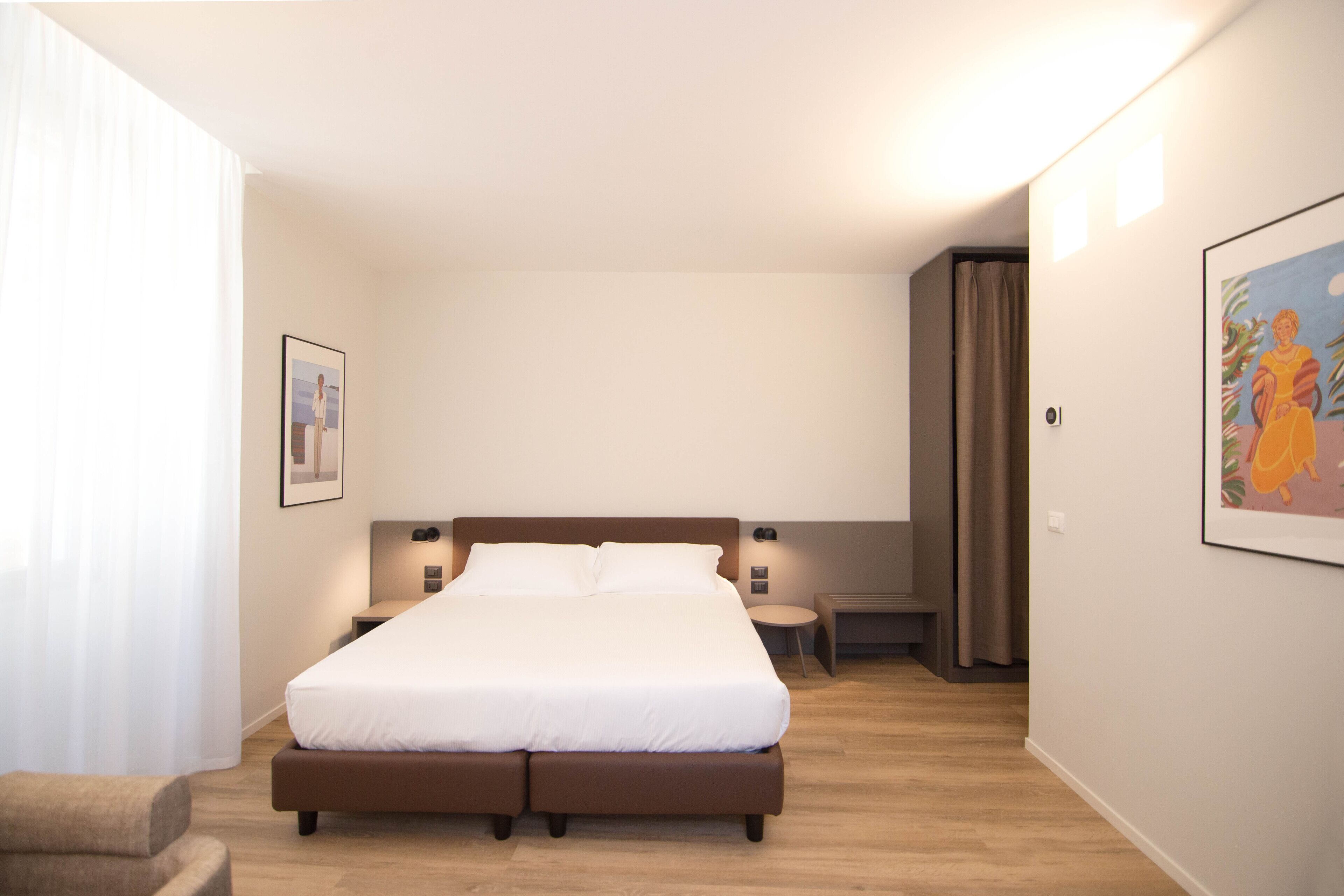 Une chambre d’hôtel moderne avec un grand lit, des tables de chevet, une chaise et des œuvres d’art accrochées aux murs.