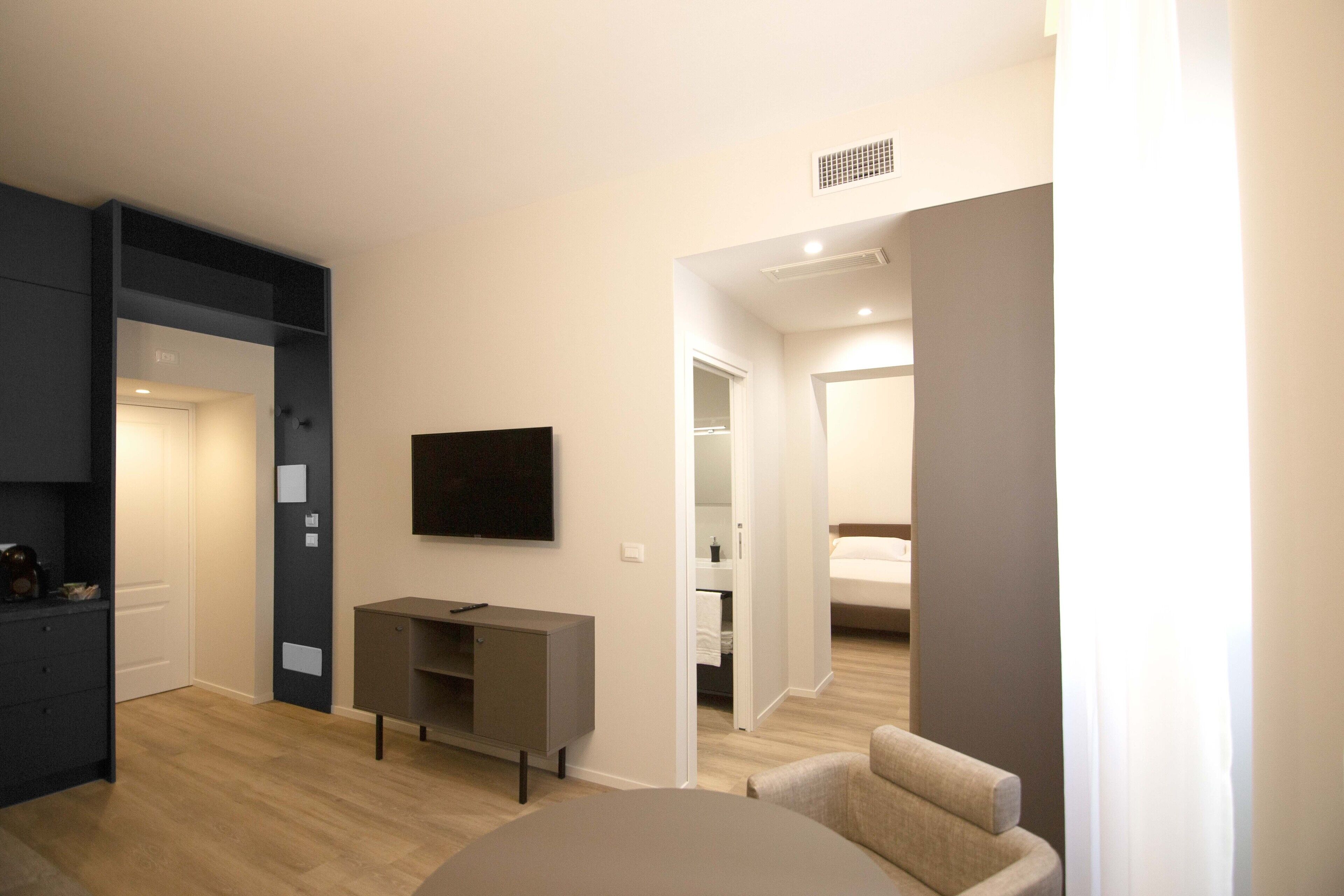 A modern living room with a flat-screen TV, a grey entertainment unit, and a beige armchair.