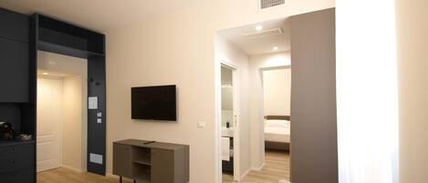 A modern living room with a flat-screen TV, a grey entertainment unit, and a beige armchair.