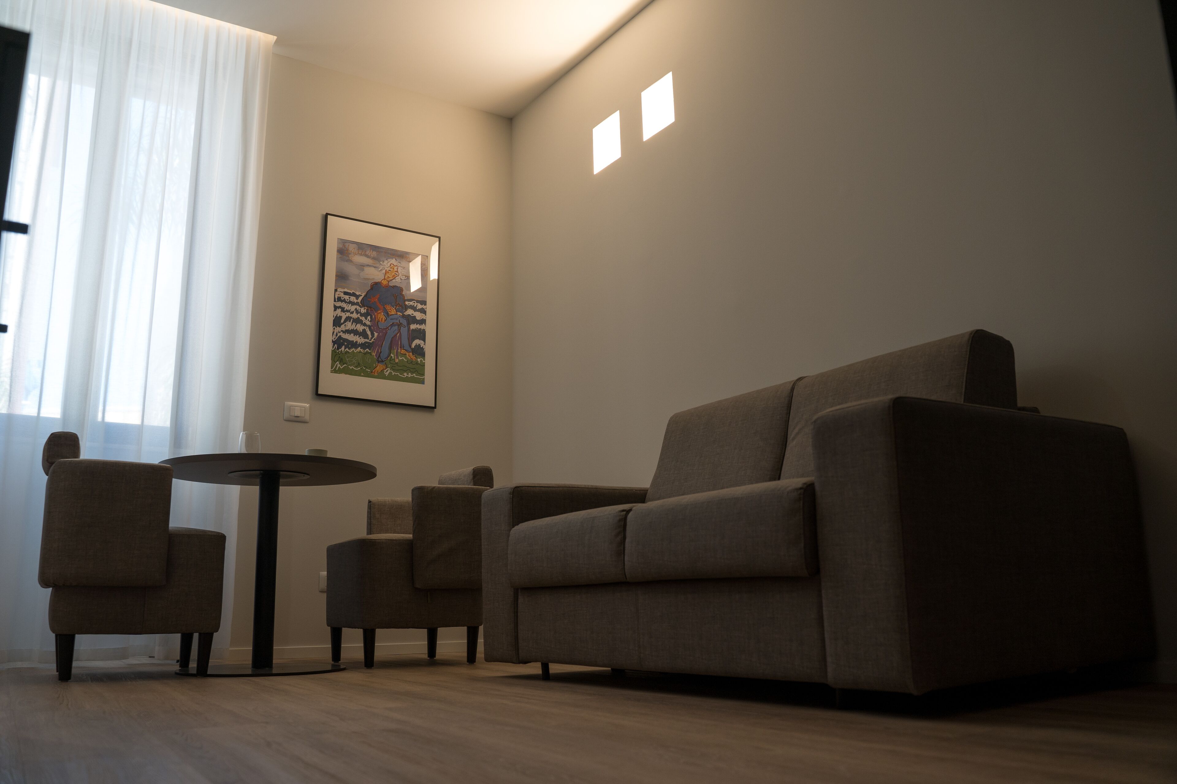 Una sala de estar con un sofá, dos sillones, una mesita redonda y un cuadro en la pared.