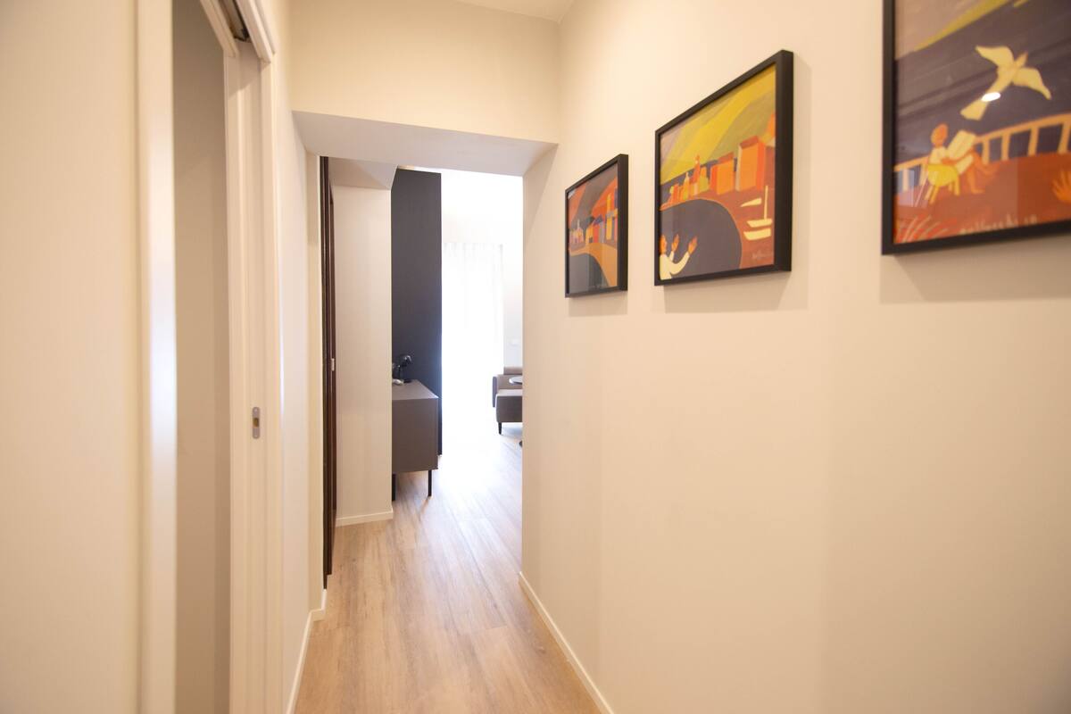 Un pasillo con suelo de madera, una puerta a la izquierda y tres cuadros en la pared derecha.