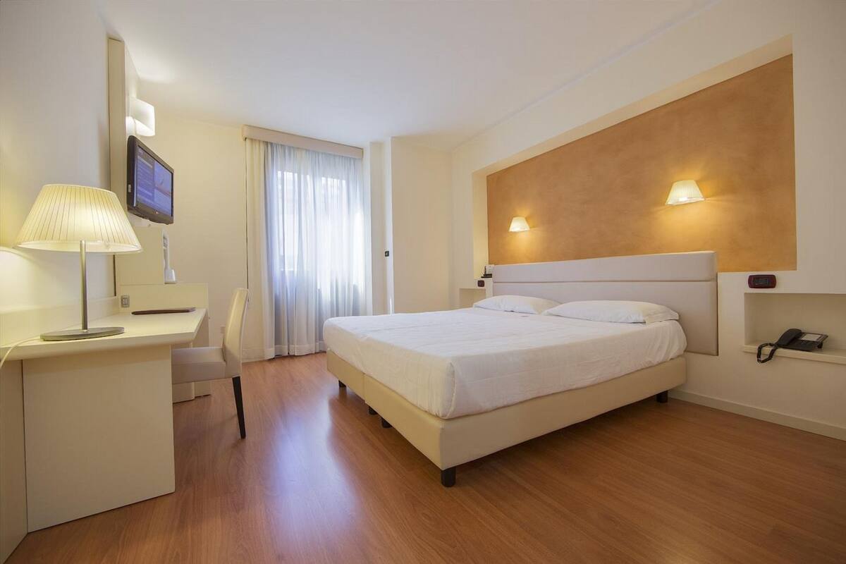 Habitación de hotel con cama, escritorio, silla y televisor instalado en la pared.