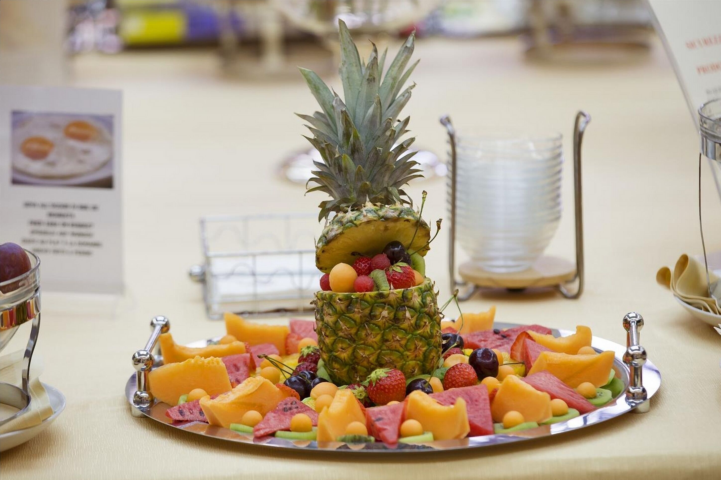 Una bandeja de plata con una piña como pieza central, rodeada de diversas frutas y queso.