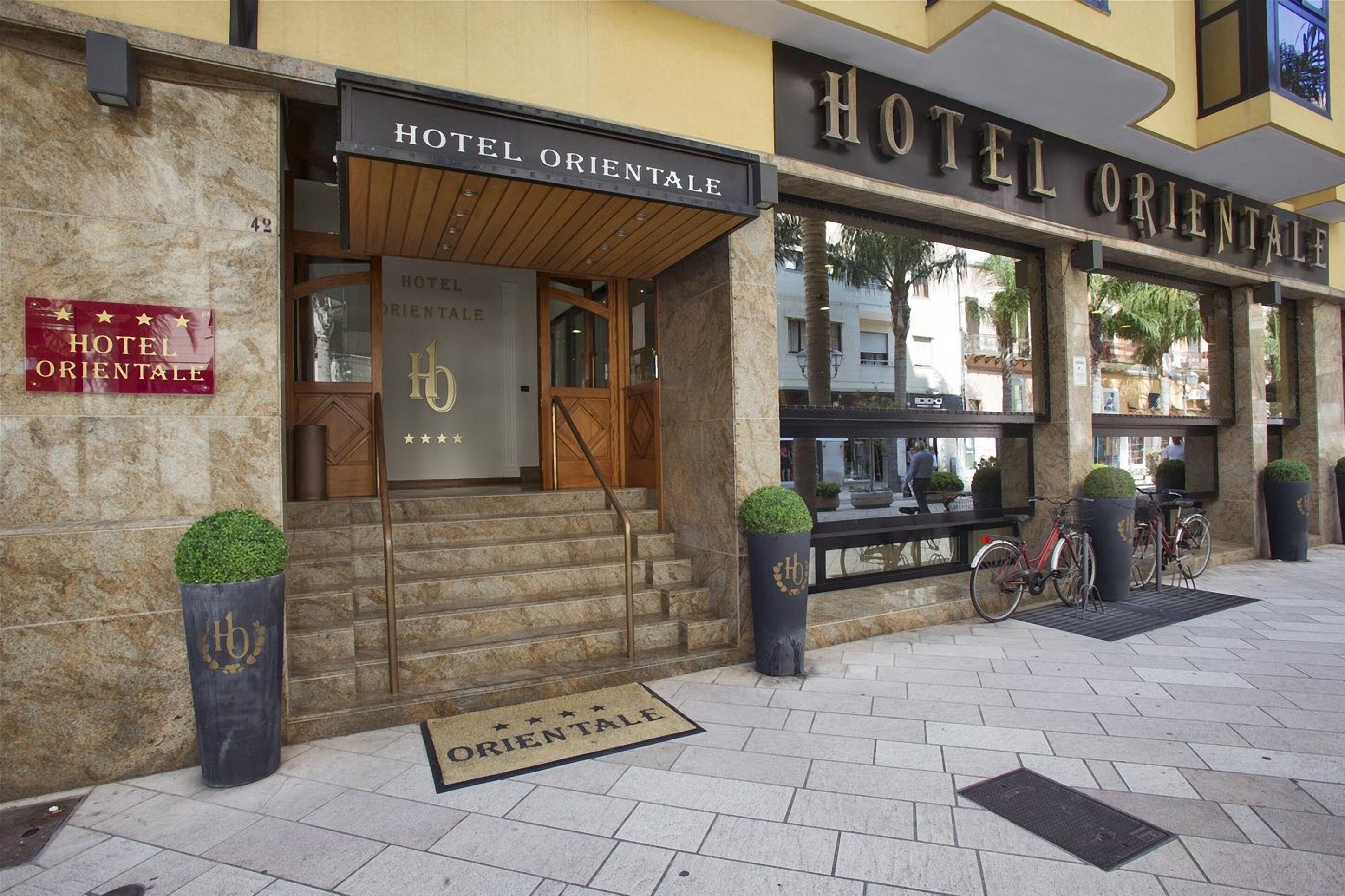 The exterior of Hotel Orientale with a stone facade, wooden entrance, and a signboard.