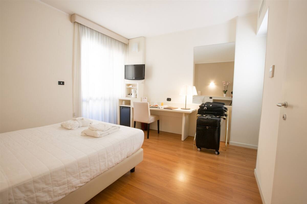Una habitación de hotel con cama, escritorio, silla y una maleta.