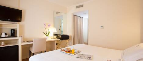 A hotel room with a bed, a desk, a television, and a breakfast tray.