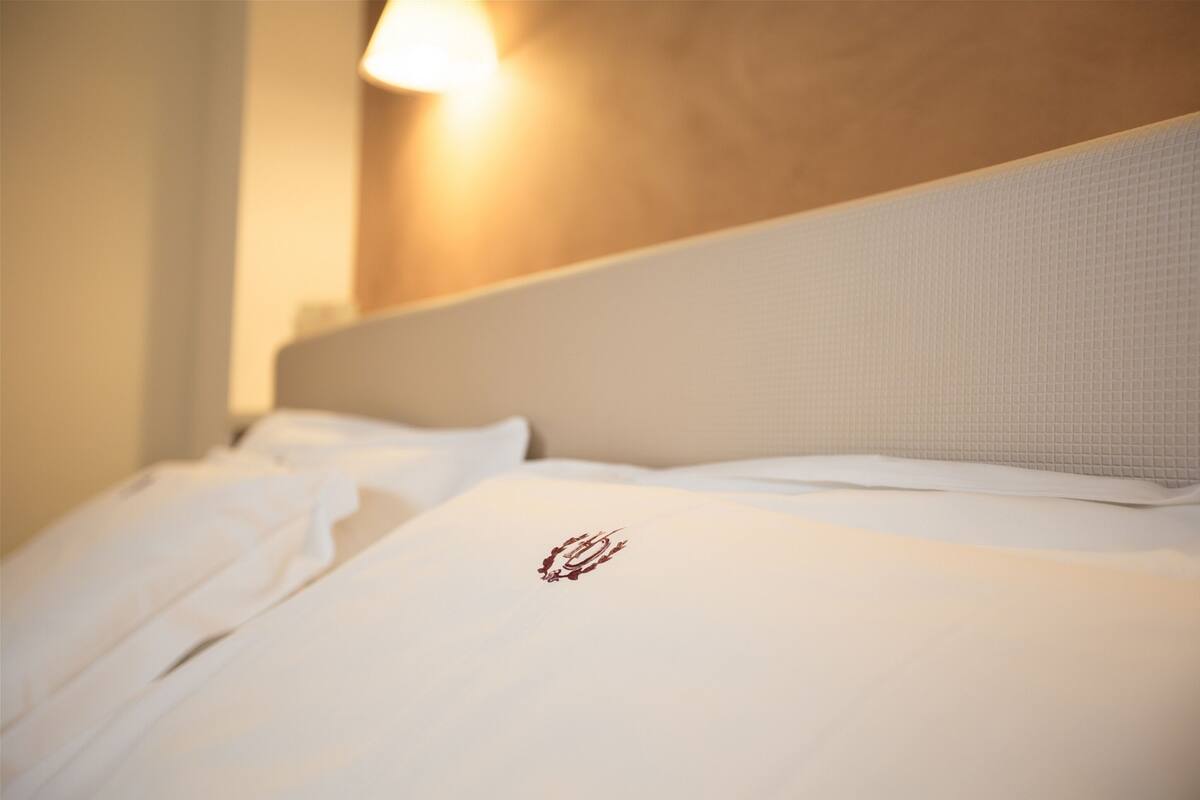 Una cama impecable con sábanas blancas y un pequeño logotipo en la almohada.