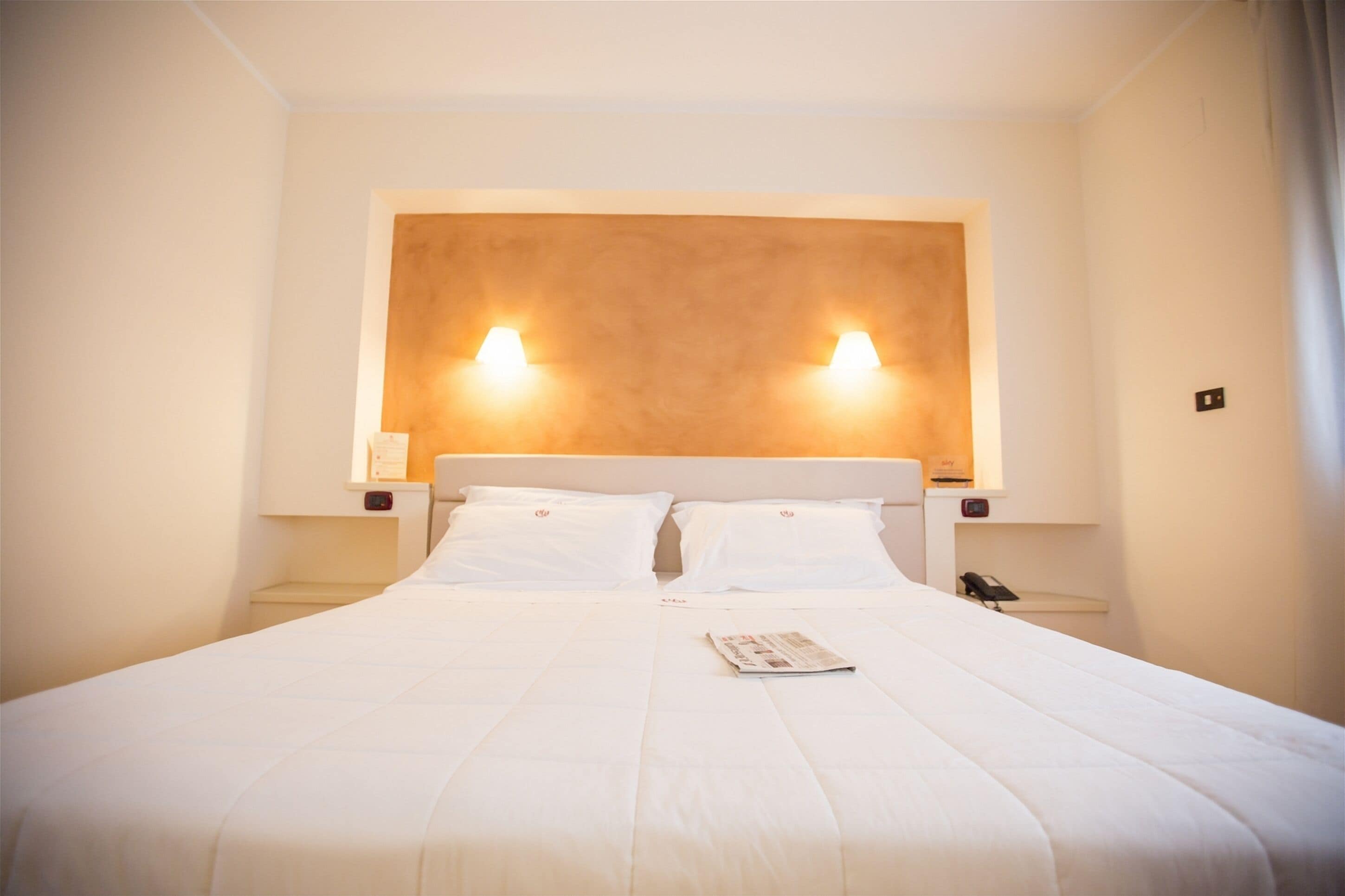 A hotel room with a large bed, two bedside lamps, a nightstand, and a telephone.