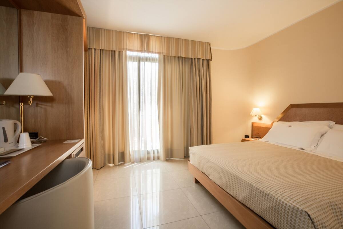 Habitación de hotel con cama, mesita de noche, lámpara y escritorio con silla.