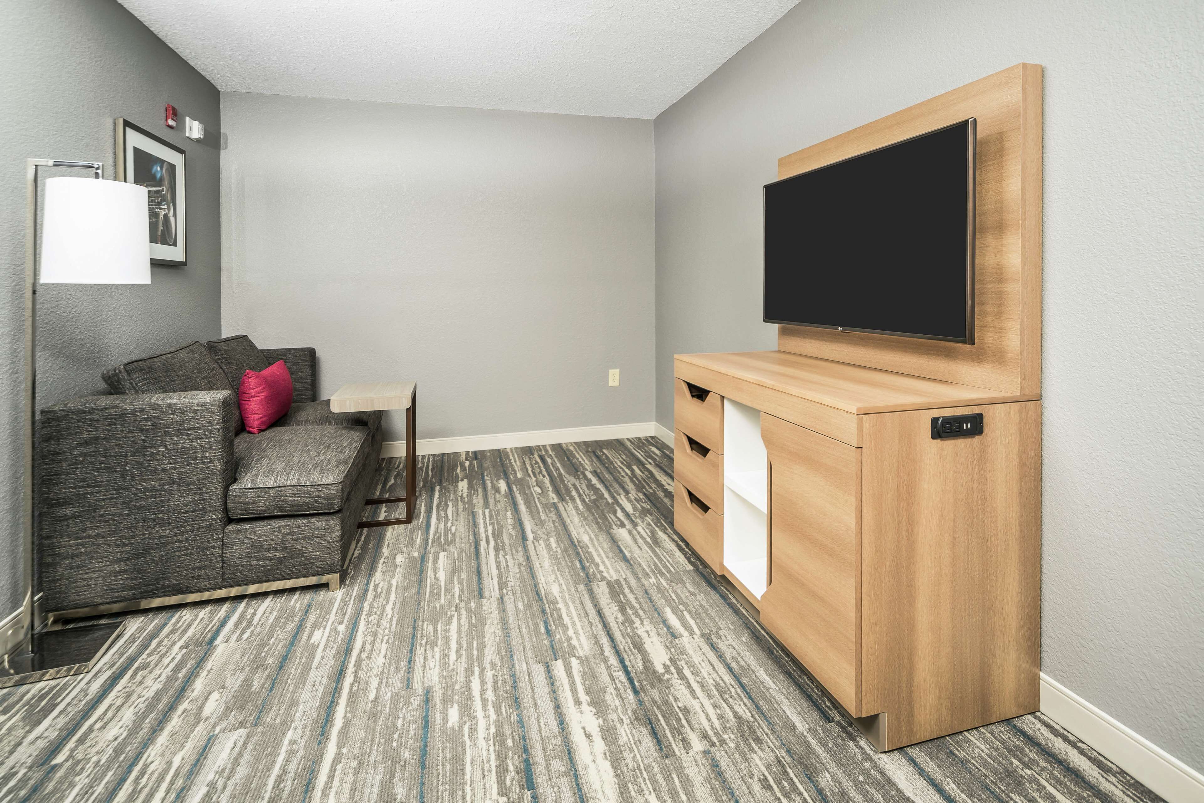 A modern living room with a grey sofa, a wooden entertainment unit, and a flat-screen TV.