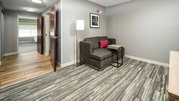 A hotel room with a grey sofa, a small table, a lamp, and a framed picture on the wall.