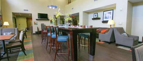 A hotel lobby with a dining area, seating arrangements, and a television mounted on the wall.