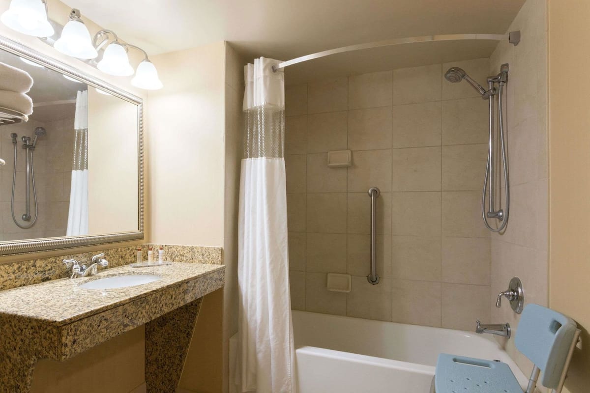 Ein Badezimmer mit Granitplatte, einem beleuchteten Spiegel, einer Dusche mit Handbrause und einer Badewanne.
