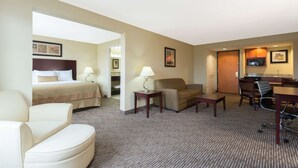 A hotel room with a bed, a sofa, a desk with a chair, and a kitchenette.