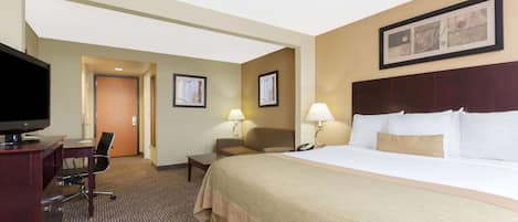 A hotel room with a large bed, a desk with a TV, two chairs, a lamp, and a framed picture on the wall.