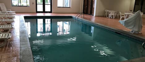 An indoor swimming pool with clear water, a 3-foot depth marker, and white lounge chairs around the pool.