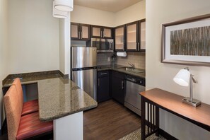 A compact kitchen with stainless steel appliances, a granite countertop, and a wooden chair. - Staybridge Suites Austin NW by IHG (Austin)