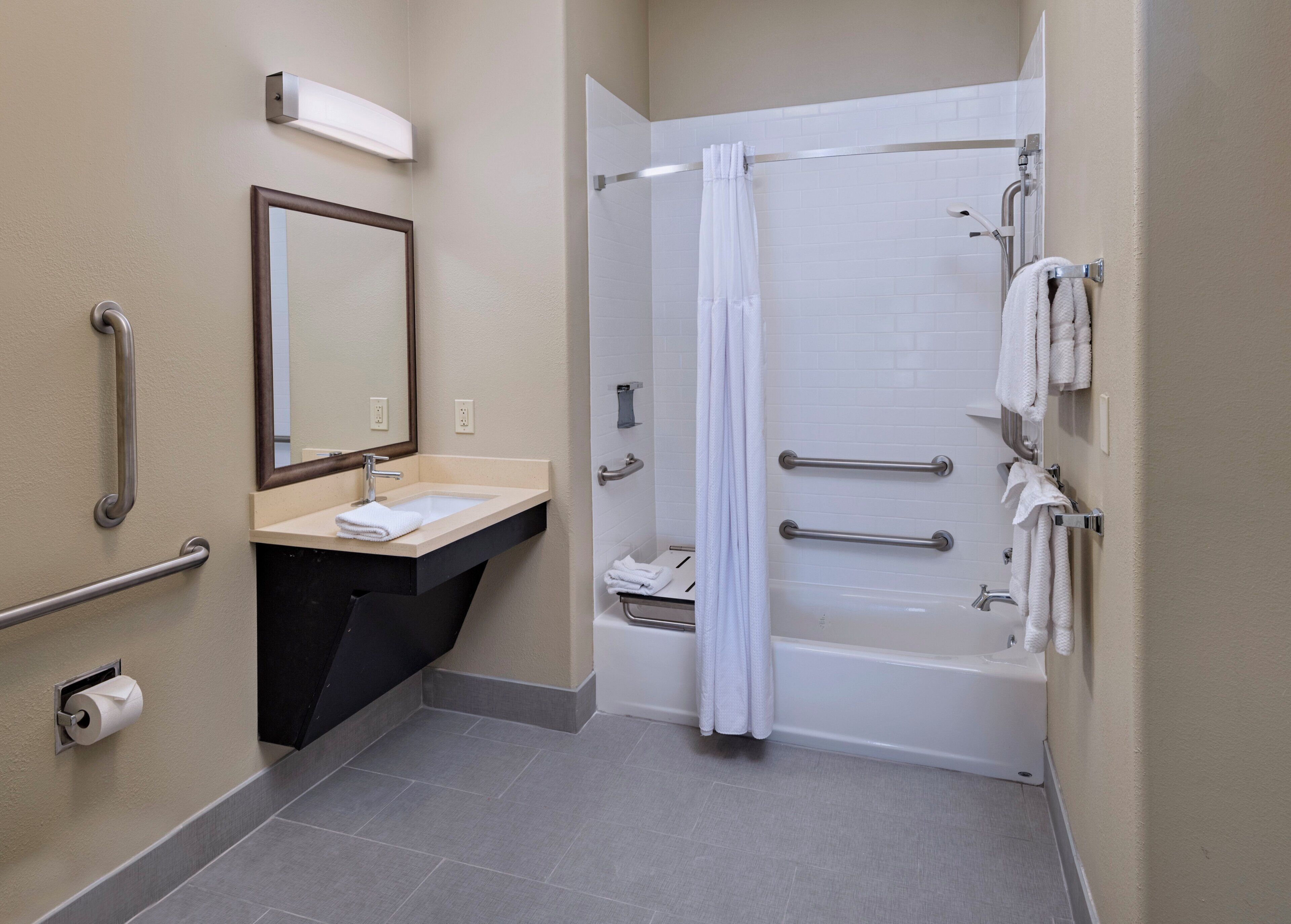 Un bagno con lavandino, specchio, portasciugamani e doccia dotata di maniglioni.