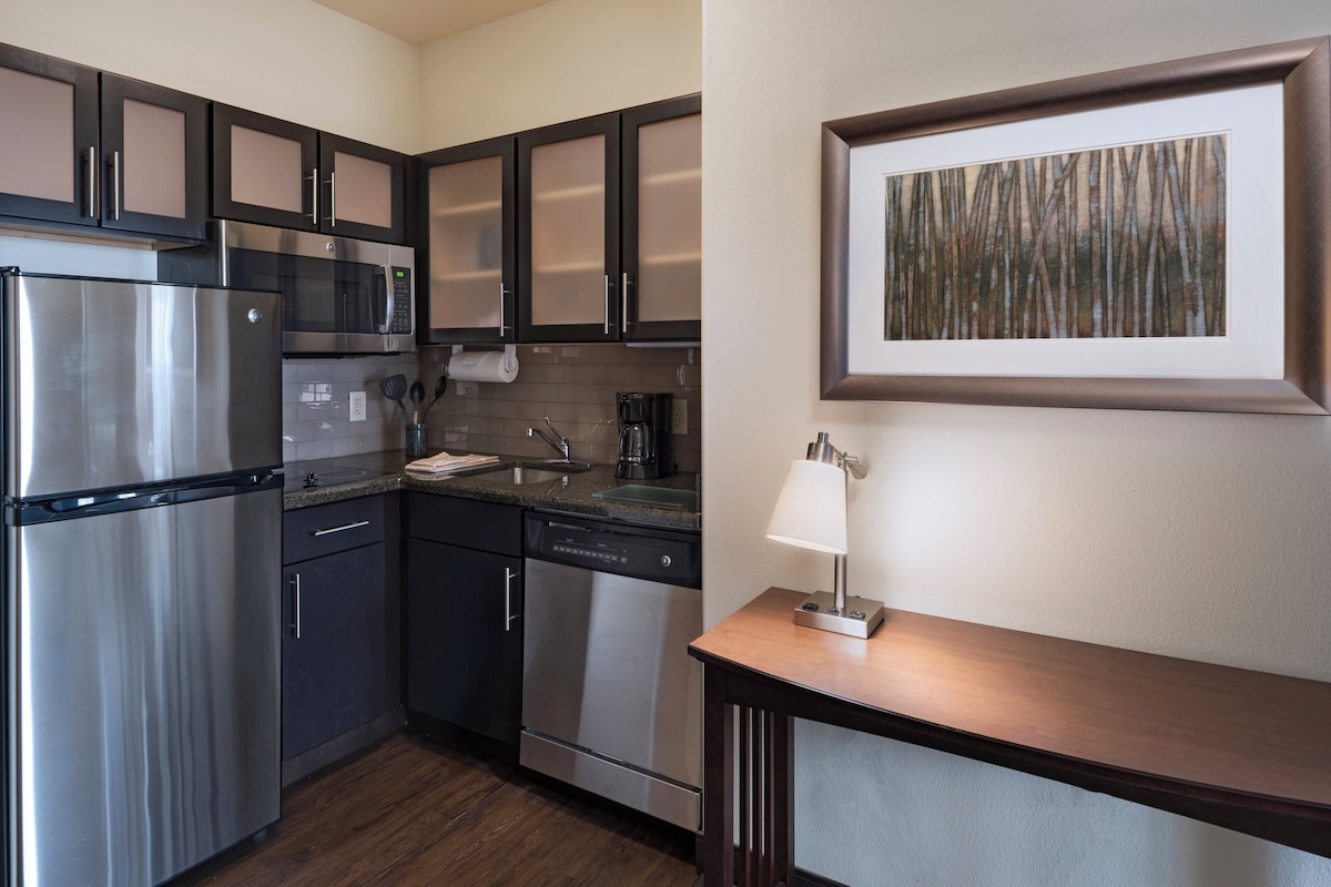 A modern kitchen with stainless steel appliances, dark cabinetry, a dishwasher, and a framed artwork on the wall.