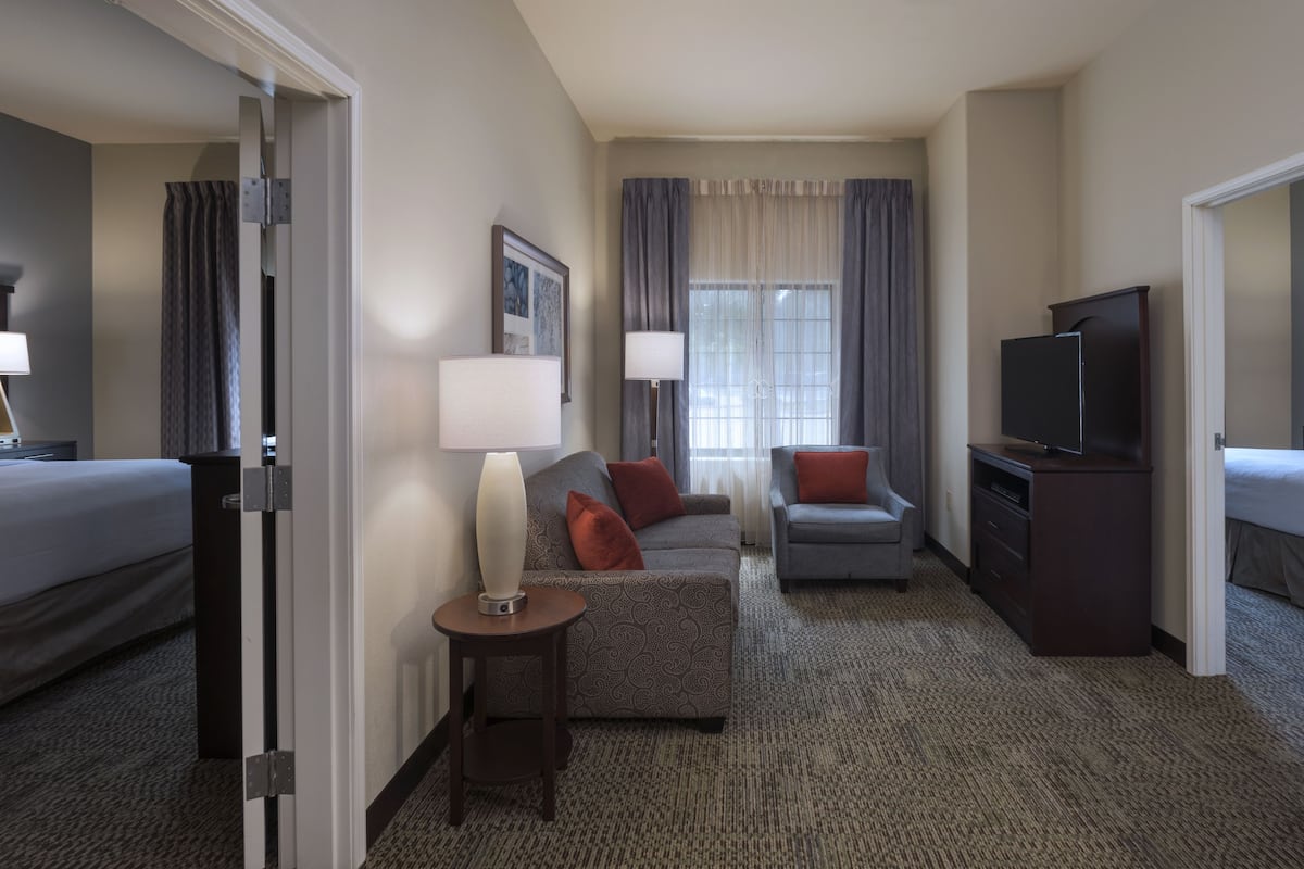 A hotel room with a bed, a sofa, a desk with a TV, and a window with curtains.