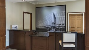 A reception area with a large framed picture of a bridge, a wooden reception desk, and a chair. - Staybridge Suites Austin NW by IHG (Austin)