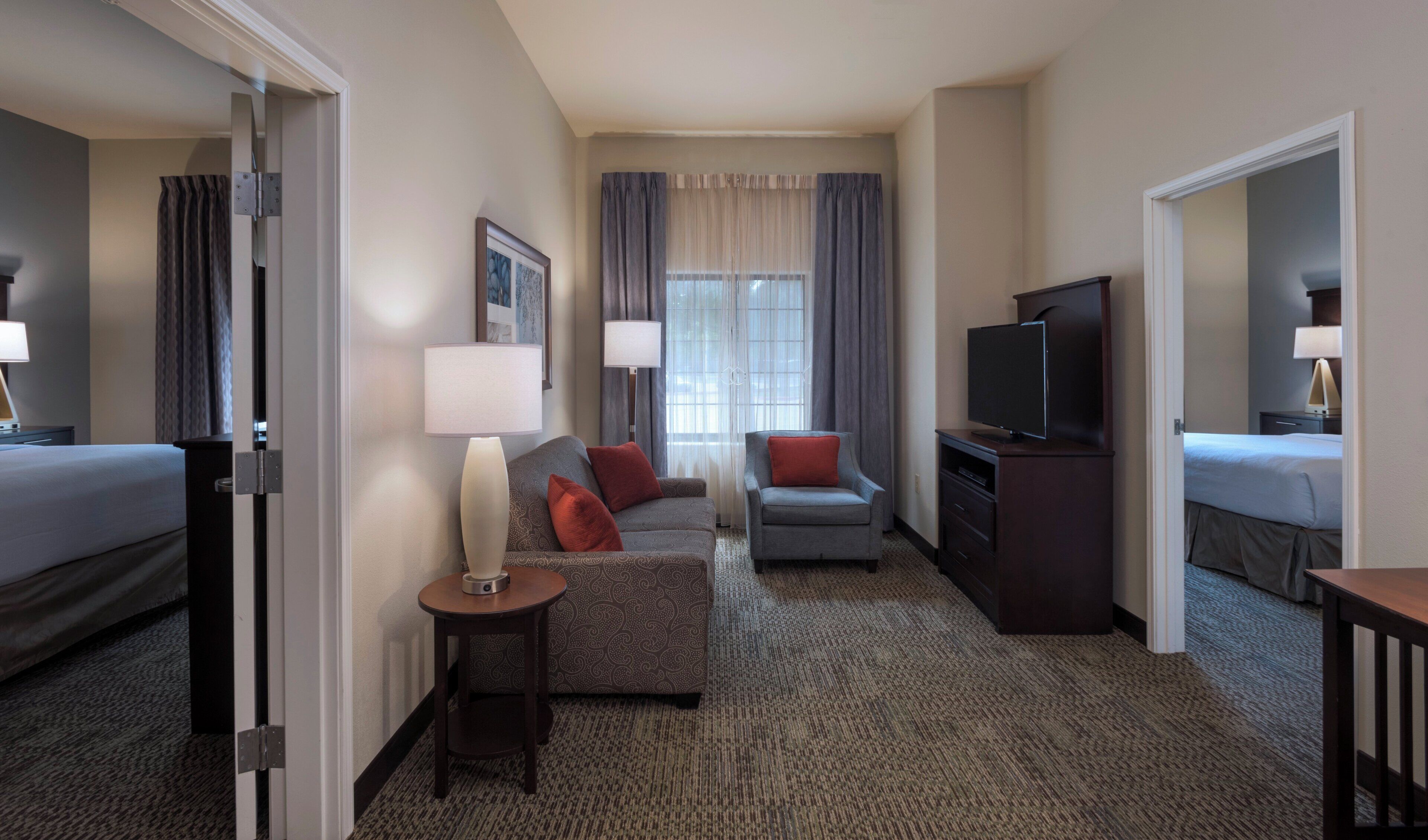 A hotel room with a bed, a sofa, a TV, a desk, and a window with curtains.