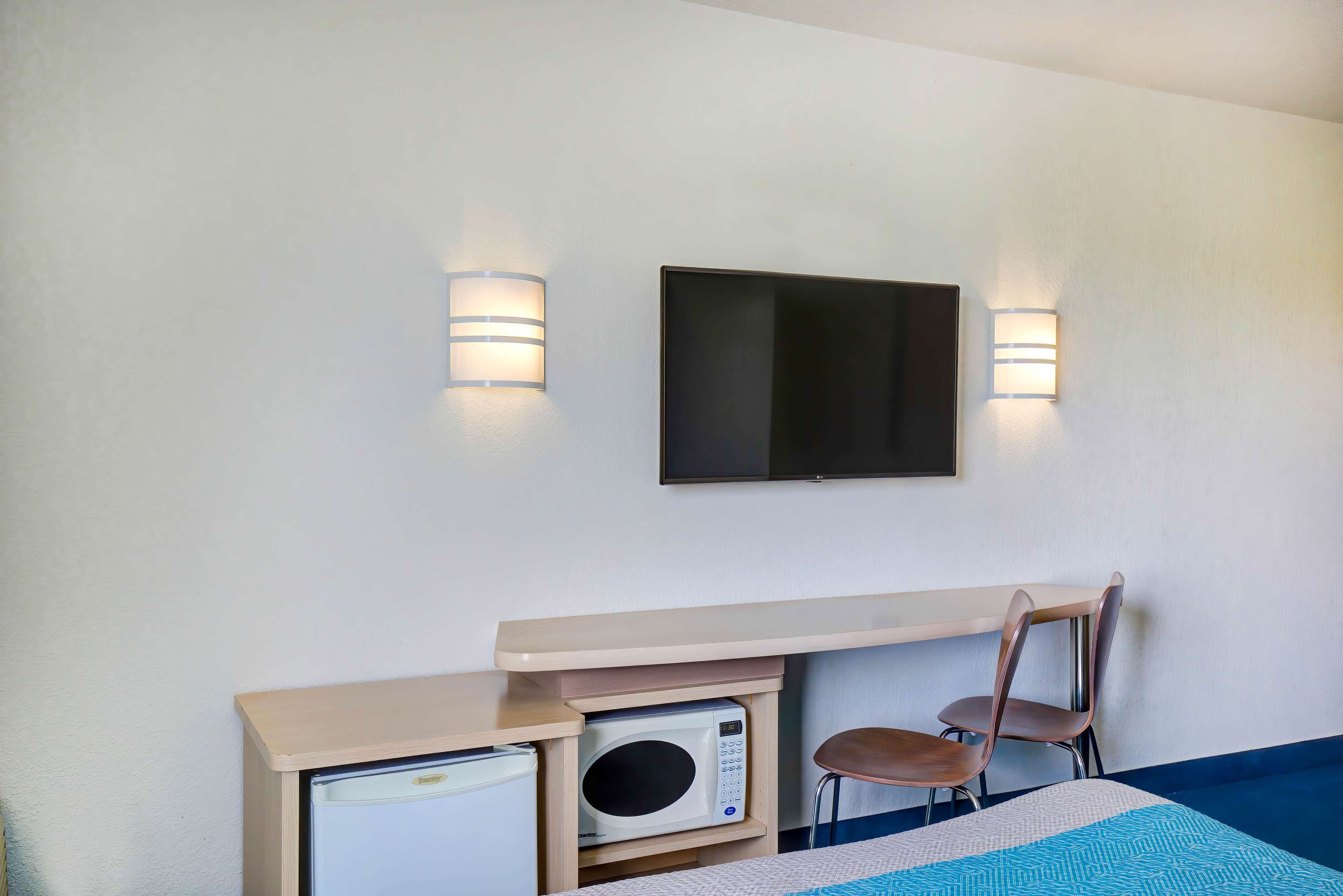 Habitación de hotel con cama, microondas, refrigerador pequeño, televisor montado en la pared y dos sillas.
