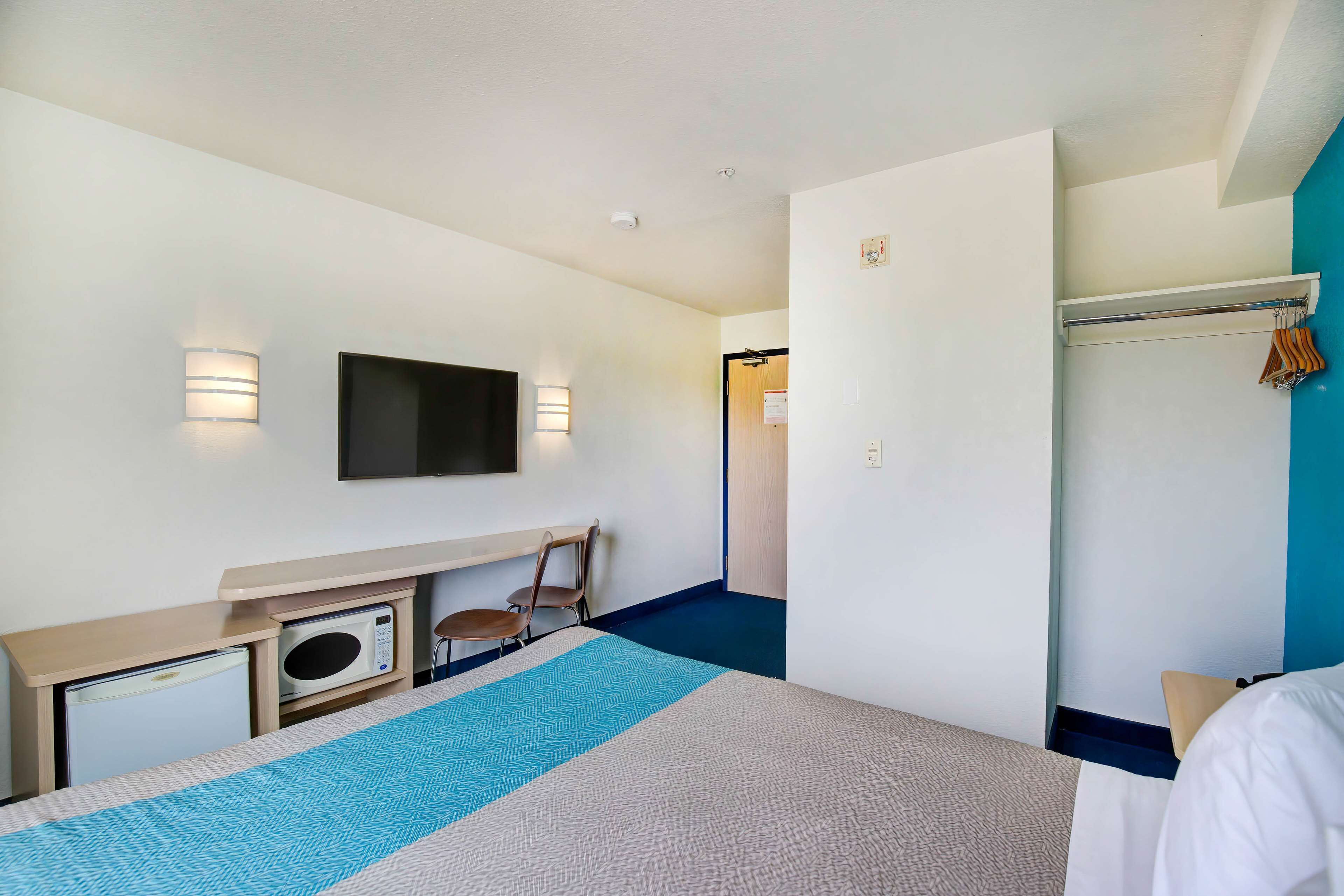 Une chambre d’hôtel comprenant un lit, un bureau avec un micro-ondes, une chaise, un téléviseur fixé au mur et un porte-manteau.