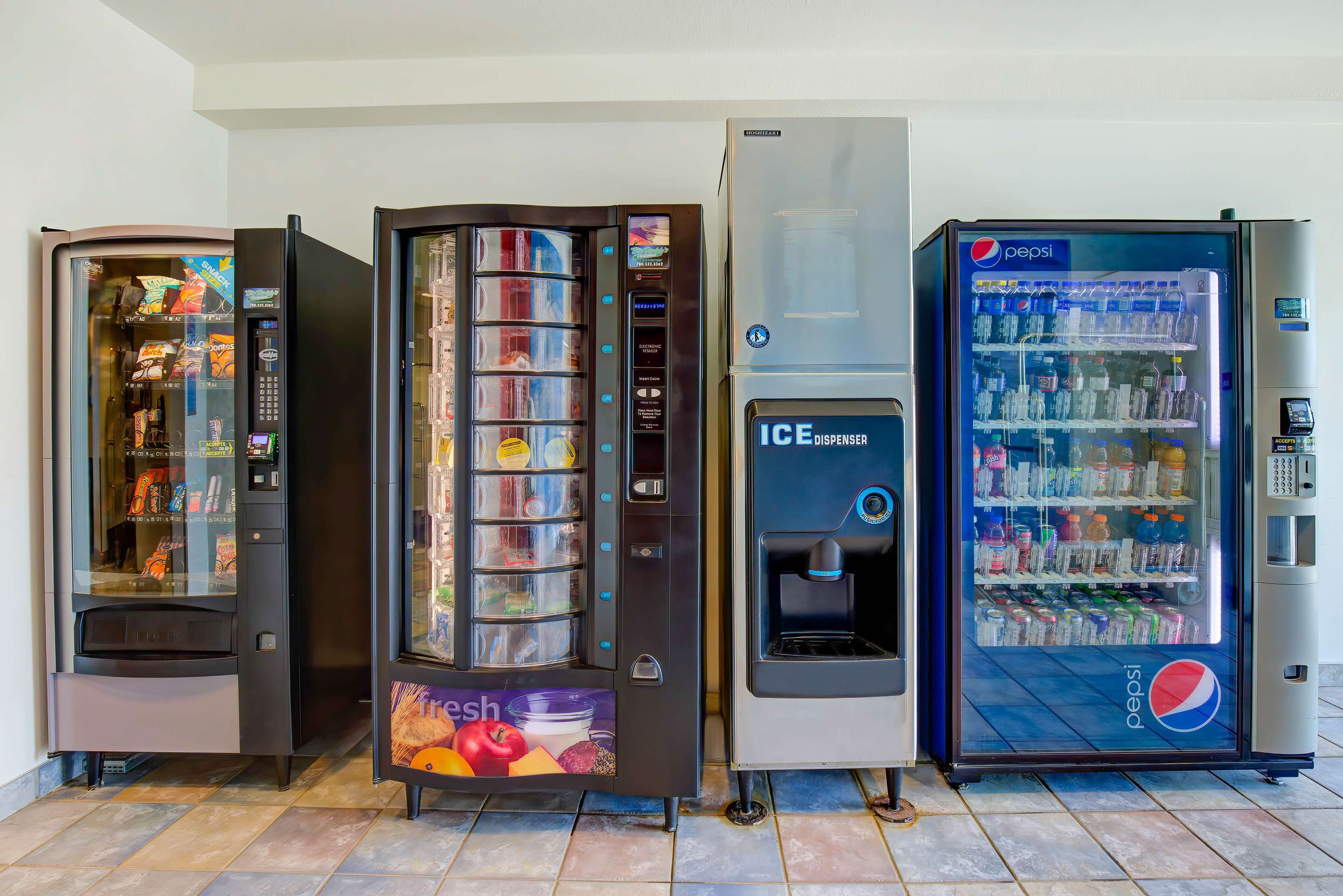 Four vending machines, including a Pepsi refrigerator and an ice dispenser, in a commercial setting.