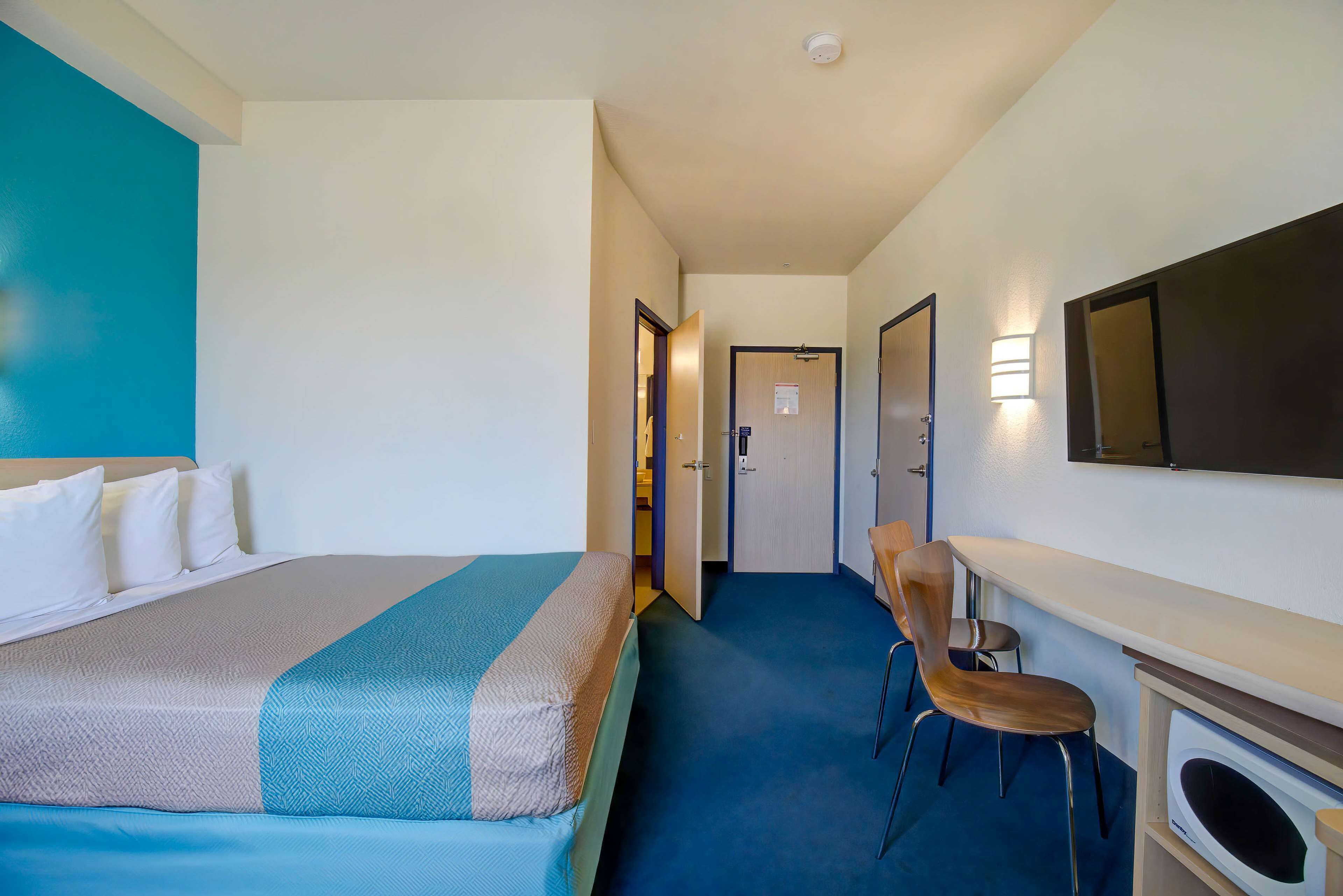 Ett hotellrum med en säng, ett skrivbord, en stol och en mikrovågsugn.