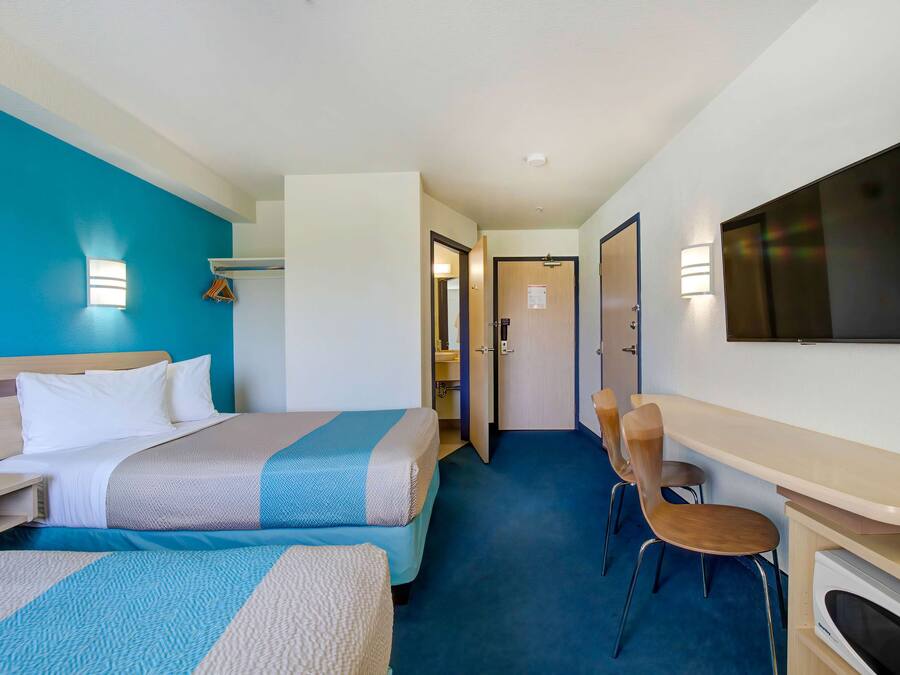 Hotelkamer met twee bedden, een bureau, een stoel, een televisie en een zichtbare badkamer door een geopende deur.