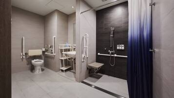 Ein modernes Badezimmer mit Toilette, Waschbecken und Duschbereich, ausgestattet mit Haltegriffen und einer Betretungsstufe.