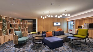 A modern lounge area with seating arrangements, a wooden bookshelf, a vending machine, and a television screen. - Holiday Inn Express Taichung Park by IHG (Taichung)