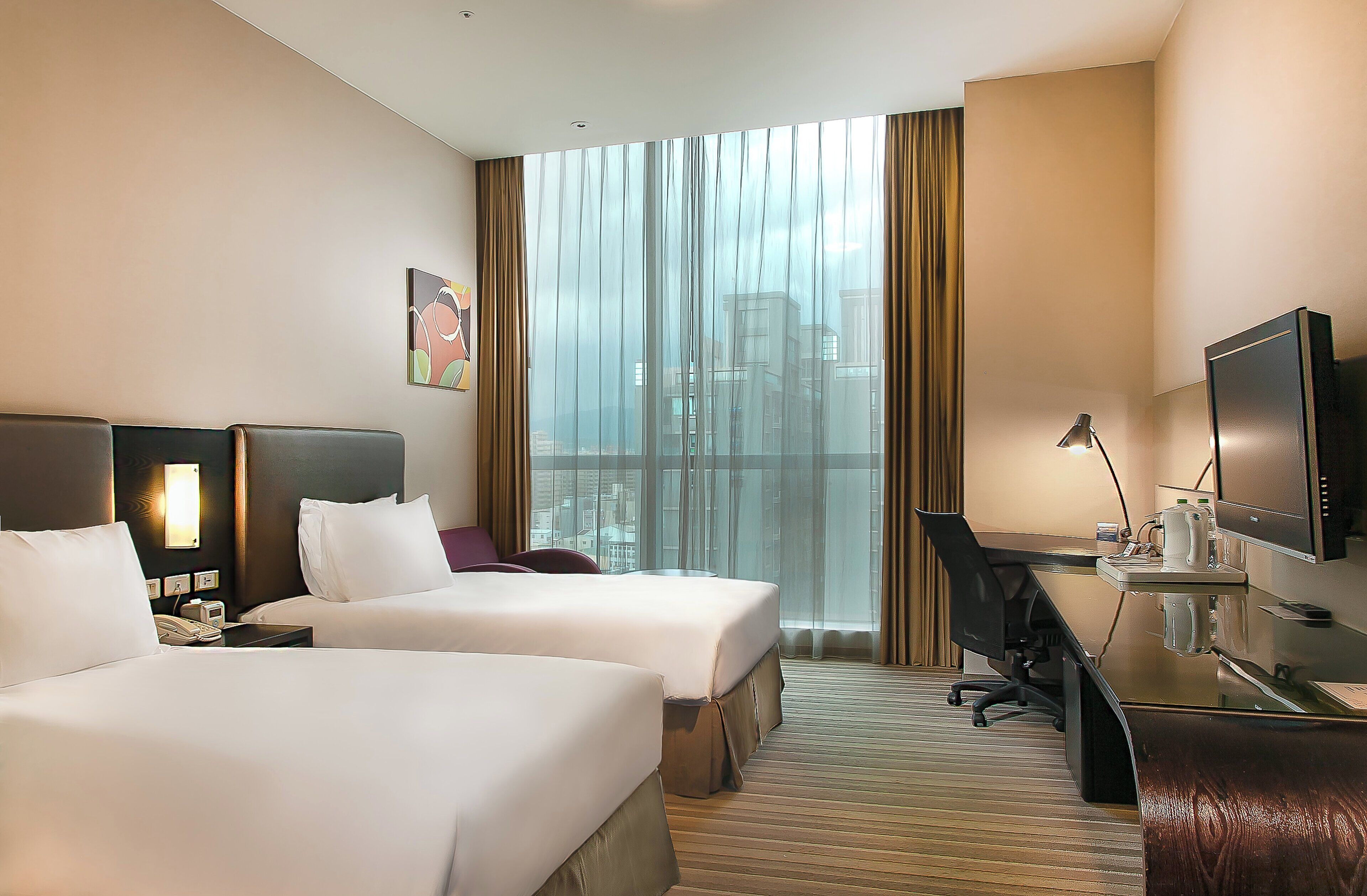 A hotel room with two beds, a desk, a chair, a television, and a large window with curtains.
