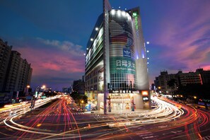 Un hôtel moderne doté d’une façade en verre incurvée remarquable, de plusieurs étages et d’une entrée bien éclairée.