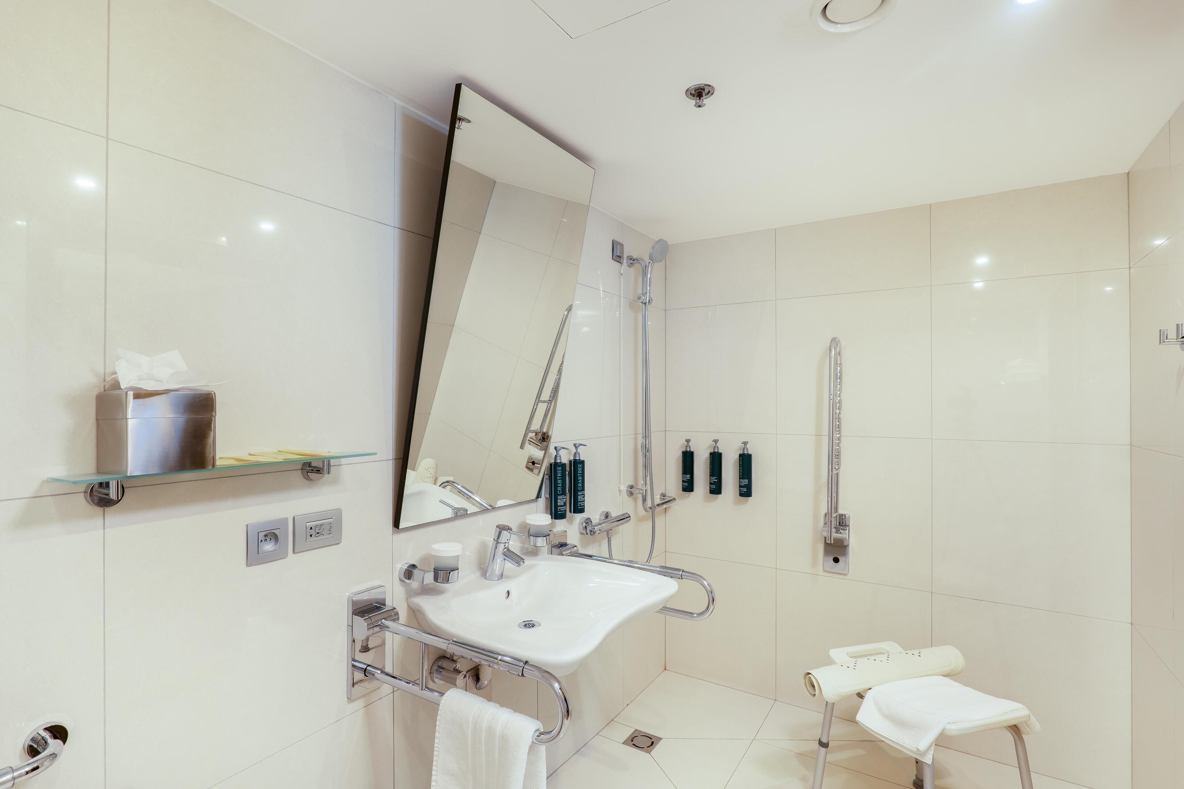 A modern bathroom with a glass shower enclosure, a white sink with a handheld showerhead, and a towel rack.