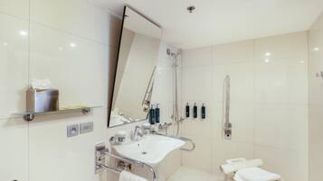 A modern bathroom with a glass shower enclosure, a white sink with a handheld showerhead, and a towel rack.