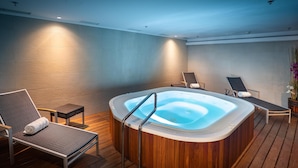 A hot tub with wooden railings, two lounge chairs, and a small table with a towel.