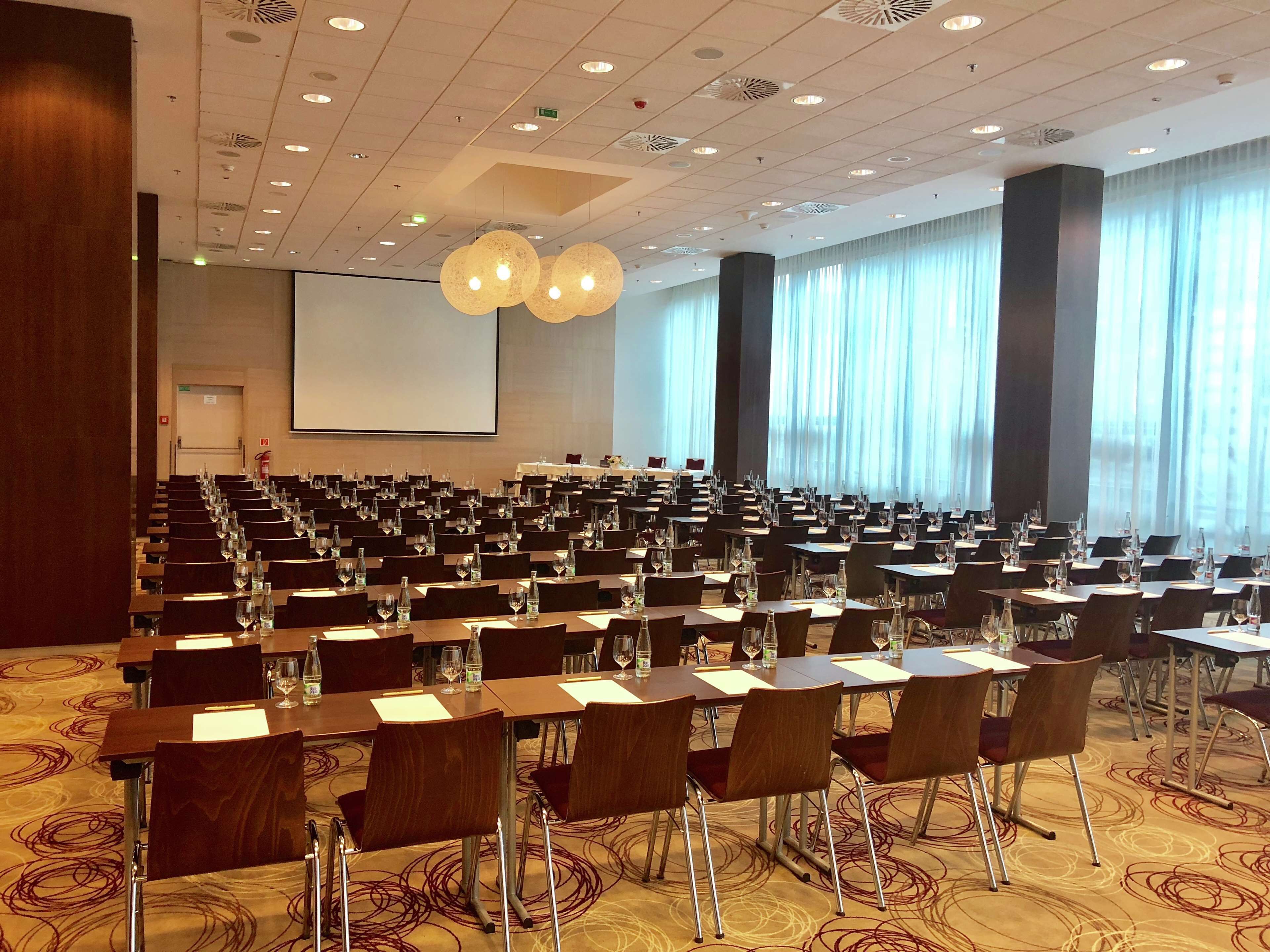 A conference room with rows of tables and chairs, a large screen, and a patterned carpet.