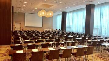 A conference room with rows of tables and chairs, a large screen, and a patterned carpet.