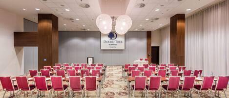 A conference room with rows of red chairs, a patterned carpet, and a ceiling with recessed lighting and a central chandelier.