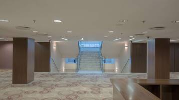 Un interior espacioso con una escalera central, alfombra estampada y columnas de madera.