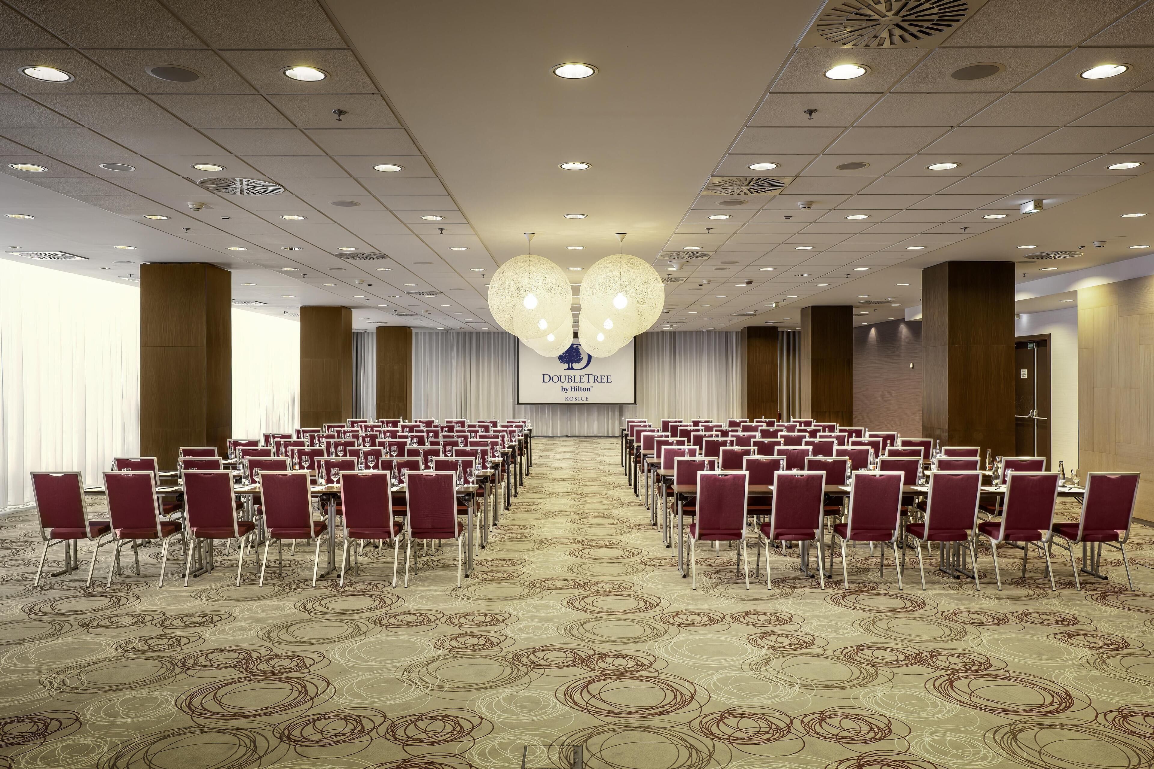 A conference room with rows of chairs, a stage with a screen, and a patterned carpet.