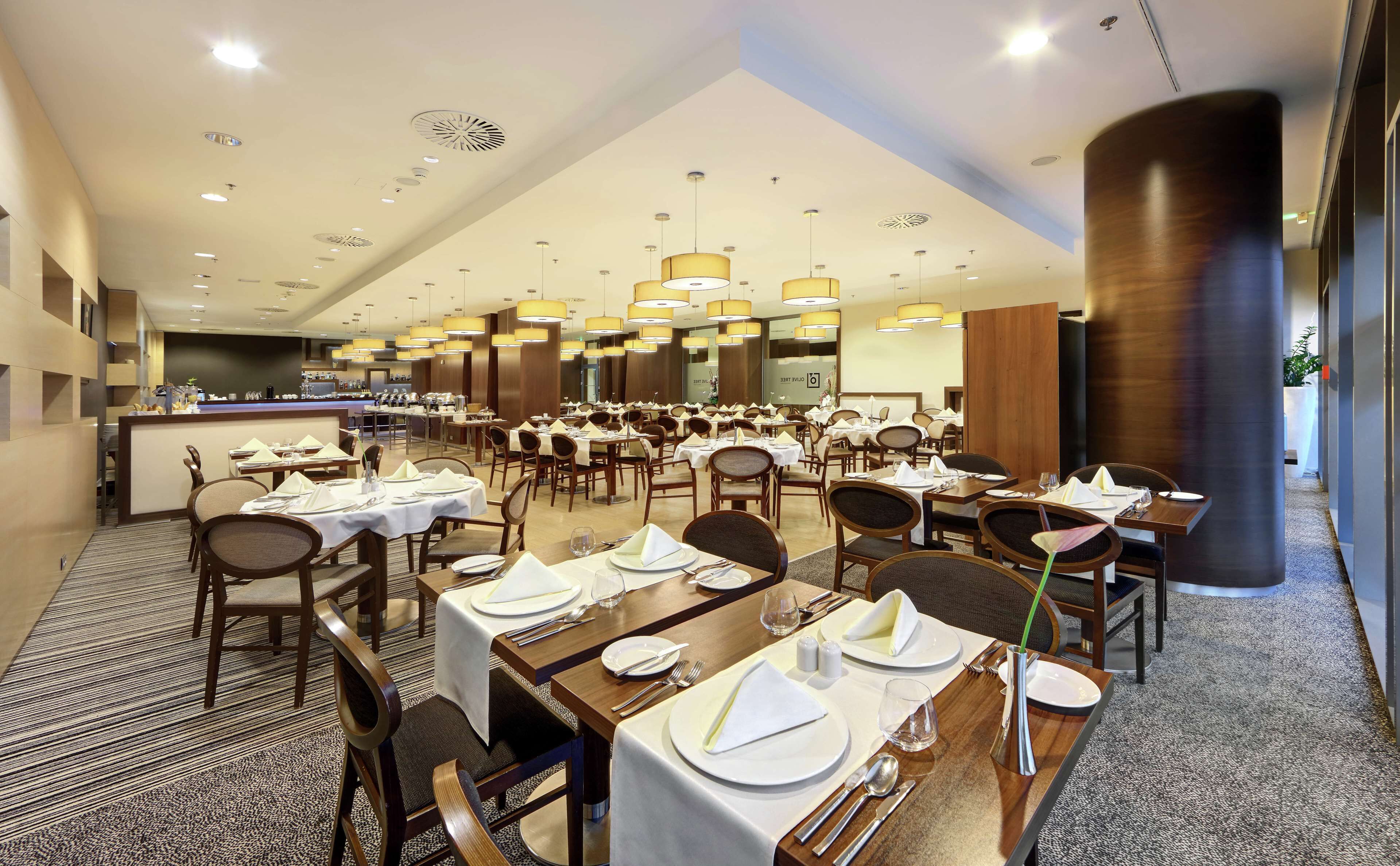 A spacious dining area with multiple tables set for guests, featuring a modern design with wooden furniture and a central bar area.