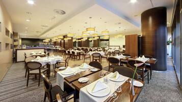 A spacious dining area with multiple tables set for guests, featuring a modern design with wooden furniture and a central bar area.