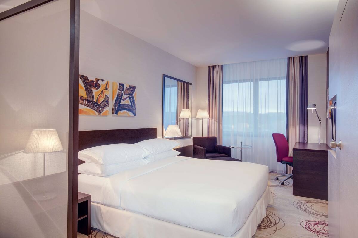 A hotel room with a large bed, a desk, two chairs, and artwork on the wall.